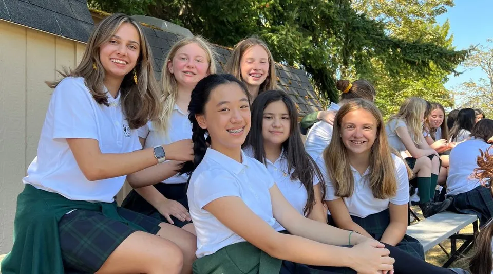 Un gruppo di studentesse sorridenti si trova all'aperto nel campus della Forest Ridge School of the Sacred Heart davanti a una vegetazione verde.