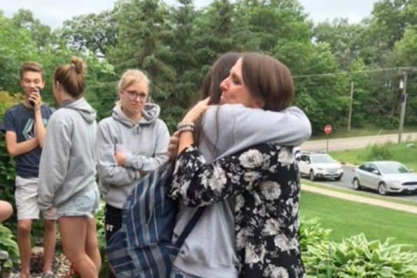 Una mujer con blusa estampada abraza a una joven con mochila en el exterior