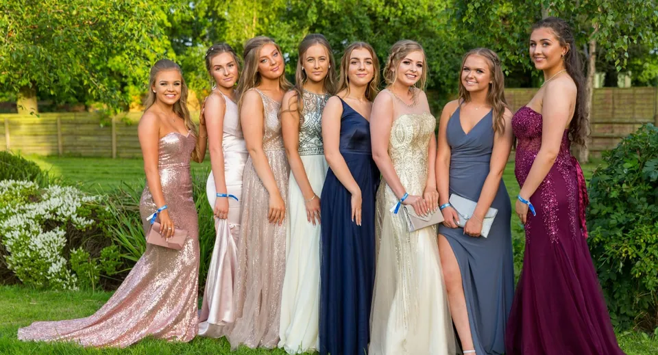 Studentesse della Bromsgrove School si trovano insieme in eleganti abiti da sera nell'area verde esterna.