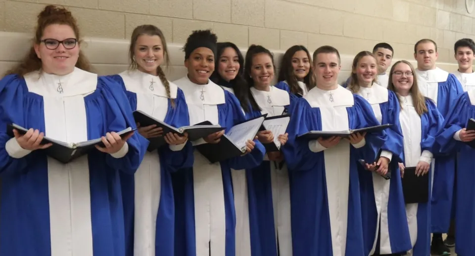 Un gruppo di studentesse della Newman Central Catholic High School si trova insieme nel corridoio con toghe di diploma blu e camicie bianche.