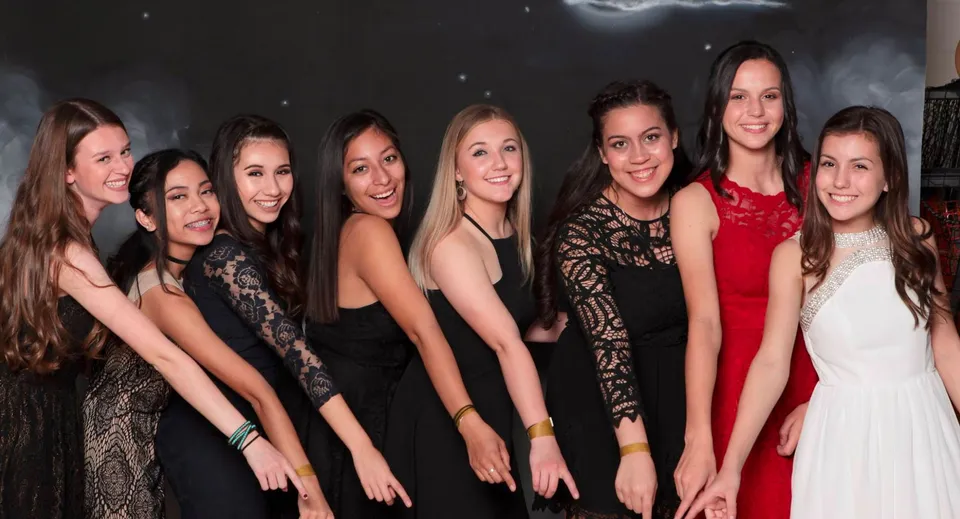 Un gruppo di giovani donne in abiti eleganti posa davanti a uno sfondo scuro con mezza luna e stelle nel campus della Heritage Christian School.