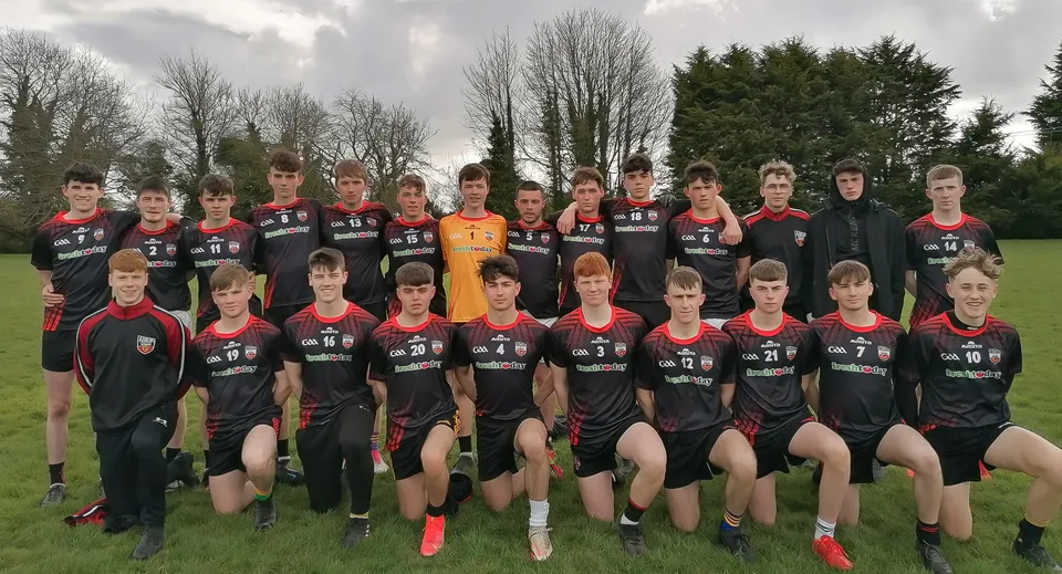 Un gruppo di studenti e studentesse dell'O’Carolan College posa insieme su un campo da calcio con alberi sullo sfondo.