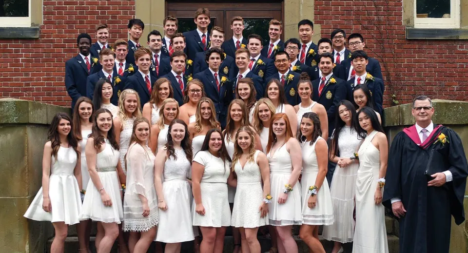 Un grande gruppo di studentesse e studenti in abiti formali davanti a un edificio in mattoni della Rothesay Netherwood School.