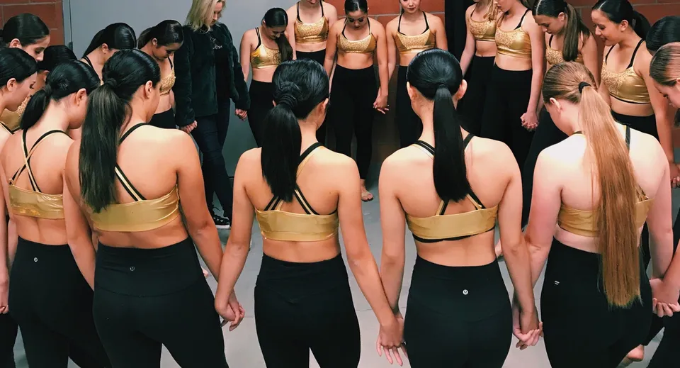 Un gruppo di giovani donne in abbigliamento sportivo nero e oro si trova in uno studio di danza nel campus del Coláiste Naomh Cormac.