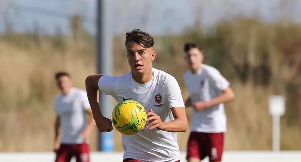 Un giocatore di calcio dell'East Sussex College Hastings corre con un pallone giallo sul campo.