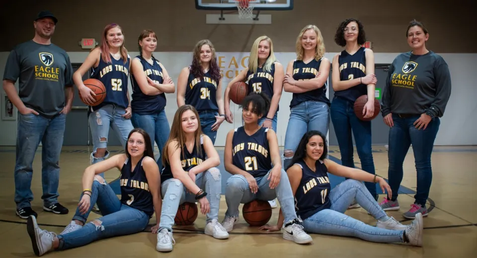 Un gruppo di studenti della Eagle School posa insieme sul campo da basket con maglie abbinate.
