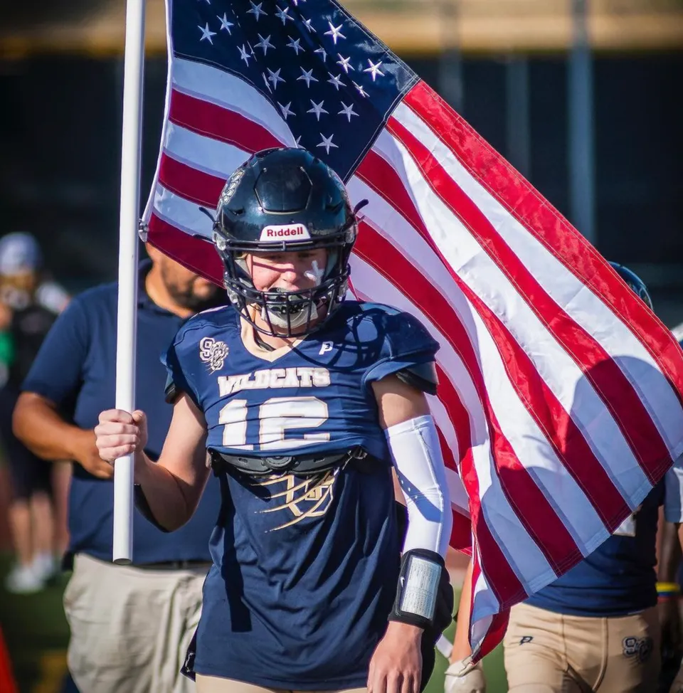 Un giocatore di football della Valencia High School tiene una bandiera americana davanti allo scenario di uno stadio.