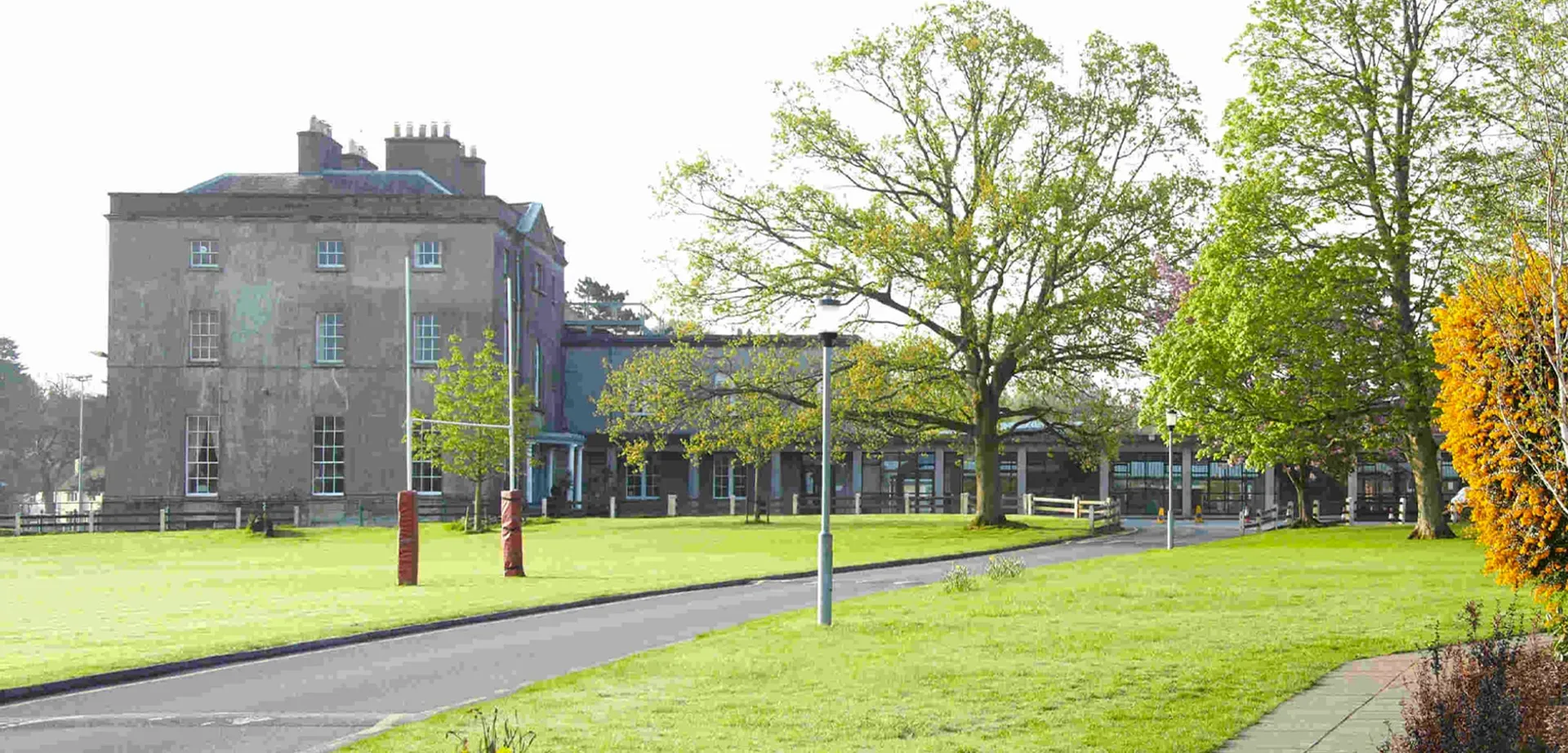Un parco erboso con alberi e un edificio storico sullo sfondo nel campus della Newtown School.
