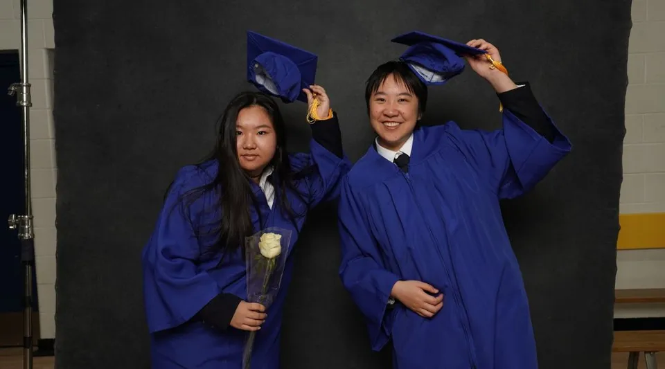 Due studenti della Royal Crown School festeggiano il diploma in toga blu su sfondo nero.