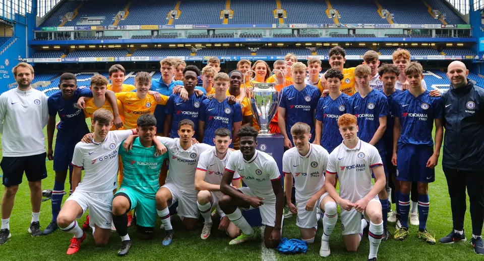 Un grande gruppo di calciatori posa sul campo sportivo del Bexhill College davanti a uno stadio.