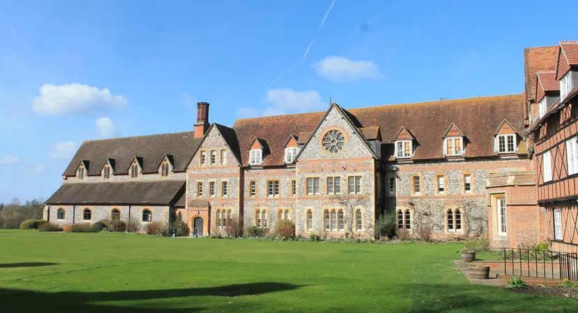 L'edificio storico in mattoni del Bradfield College si erge su un prato curato sotto un cielo blu.