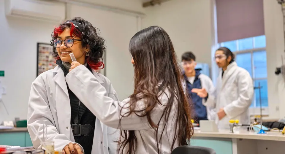 Studenti e studentesse del David Game College lavorano in un laboratorio indossando camici da laboratorio e occhiali protettivi.