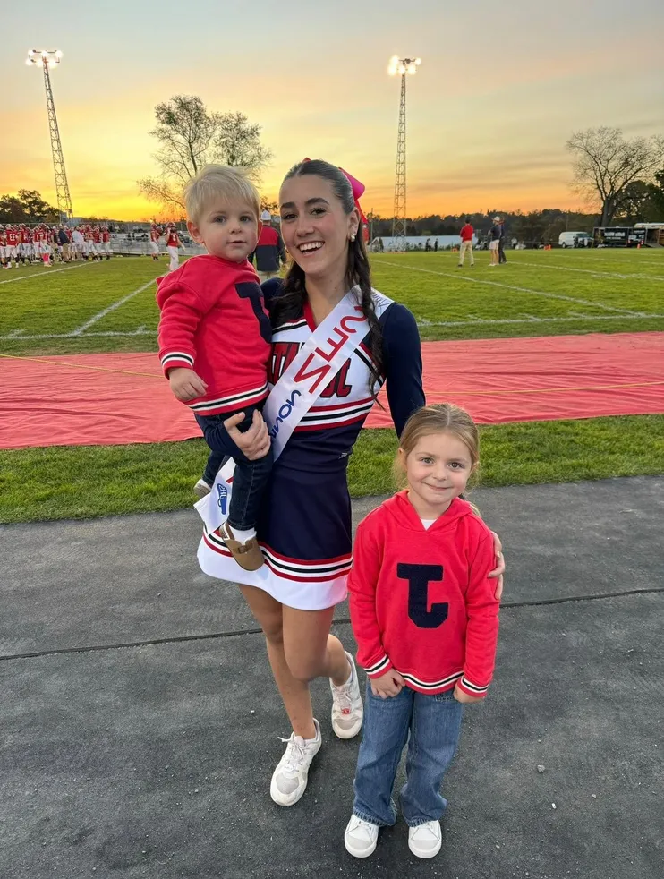 Studentessa in divisa da cheerleader con due bambini a bordo di un campo di football di una high school americana