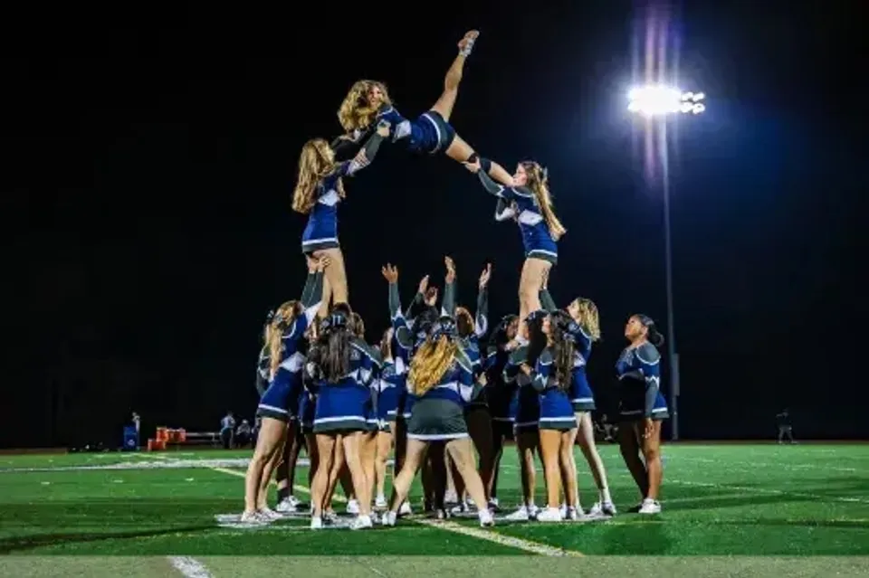 Studenti e studentesse della St. Mary's Ryken High School formano una piramide di cheerleader sul campo da football sotto i riflettori.