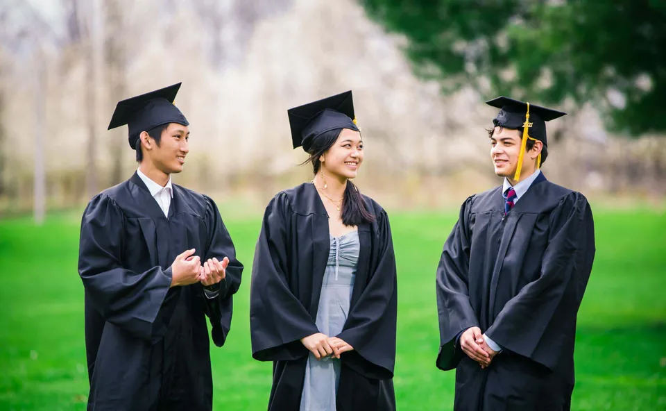 Tre diplomate e diplomati della Northern Academy stanno all'aperto su un prato con le loro toghe da diploma.