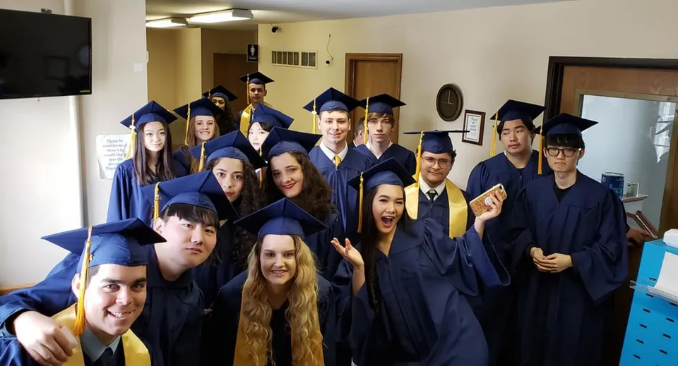 Un gruppo di diplomati della Eagle School in toghe blu da diploma in una stanza con televisore e mobili.