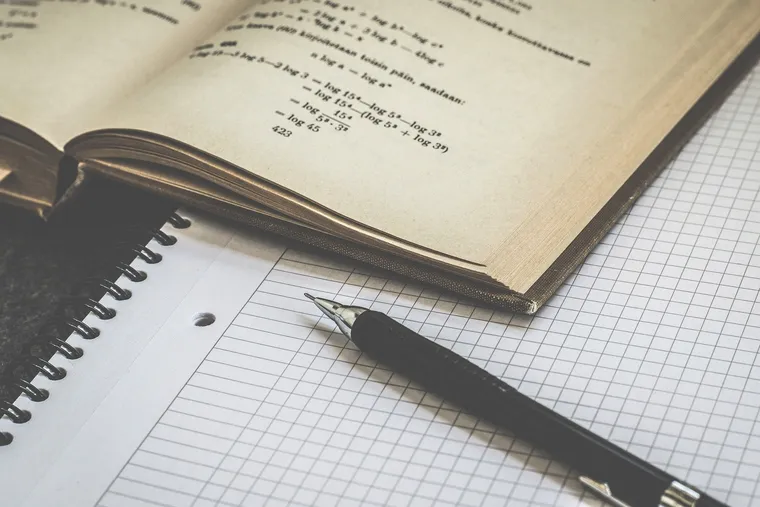 Aufgeschlagenes Mathebuch mit Formeln, Füller und kariertem Collegeblock