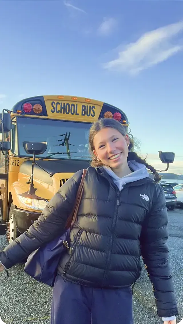 Studentessa sorridente davanti a uno scuolabus giallo