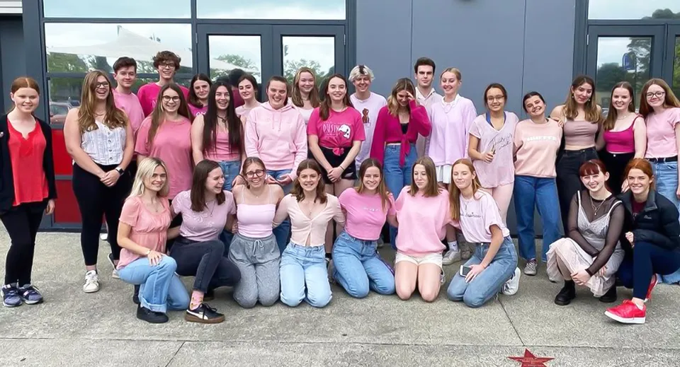 Un gruppo di giovani donne vestite in diverse tonalità di rosa posa davanti a un edificio moderno del Selwyn College.