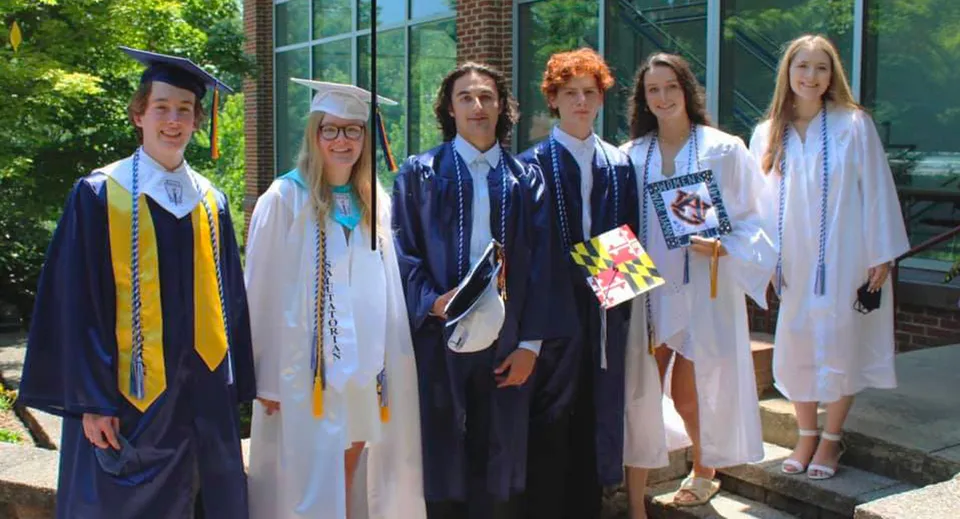 Un gruppo di diplomati della The Calverton School sta in abiti accademici davanti a un edificio in mattoni con grandi finestre e piante verdi.