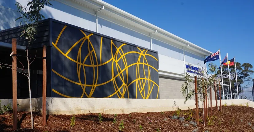 L'ampio edificio bianco con un murale astratto giallo nel campus del Wanneroo Secondary College sotto un cielo blu.