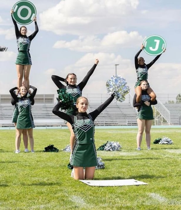 Squadra di cheerleader in divisa verde si esibisce sul campo sportivo di una high school americana