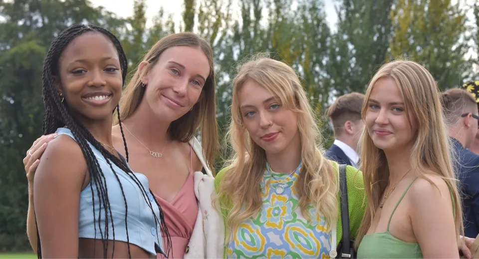 Quattro studentesse di The High School posano sorridenti all'aperto davanti ad alberi e aree verdi.
