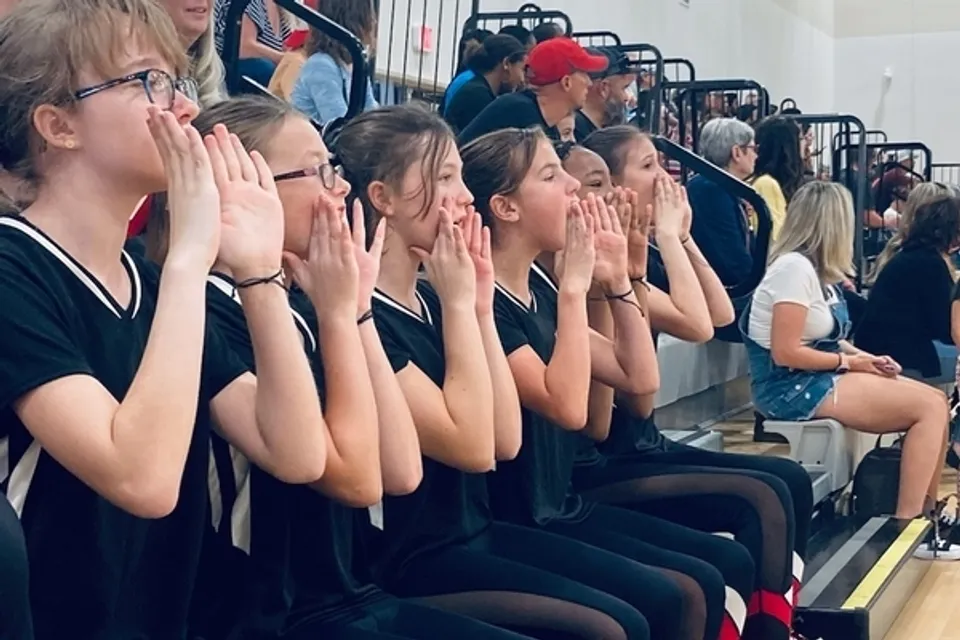 Diverse studentesse della Parkhurst Academy siedono sugli spalti e gridano con le mani intorno alla bocca.