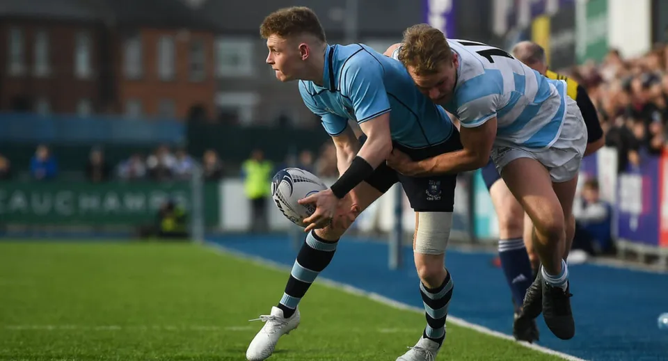 Un giocatore di rugby della John Scottus Secondary School tiene il pallone durante un placcaggio sul campo.