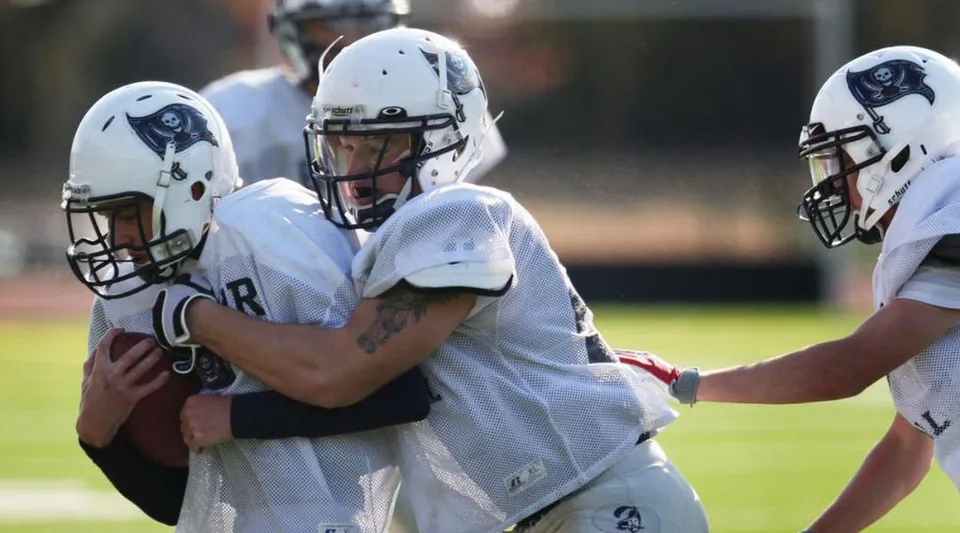 Un gruppo di giocatori di football in uniformi bianche in piedi su un campo erboso nel campus della Blair Academy.