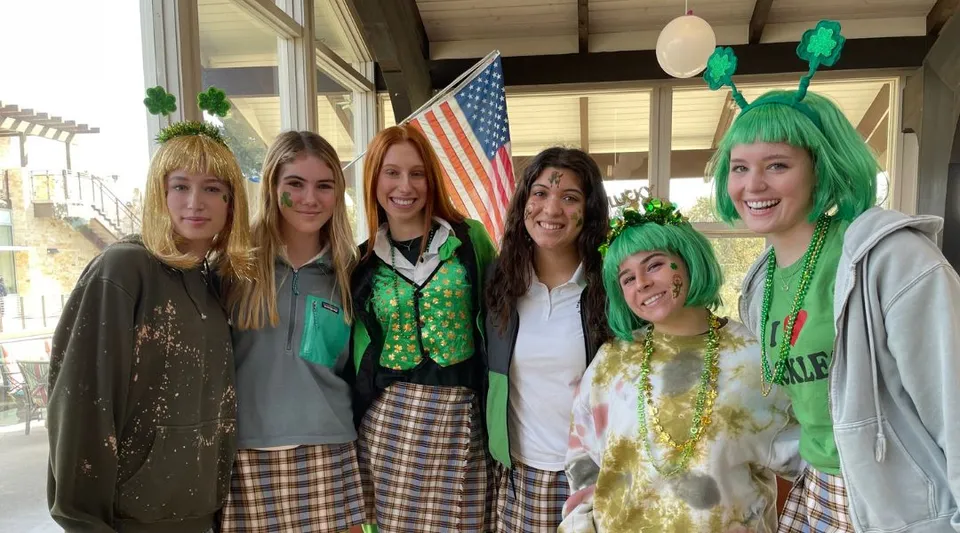 Un gruppo di donne in abiti da festa si mette in posa davanti a una bandiera americana nel campus della Santa Catalina School.