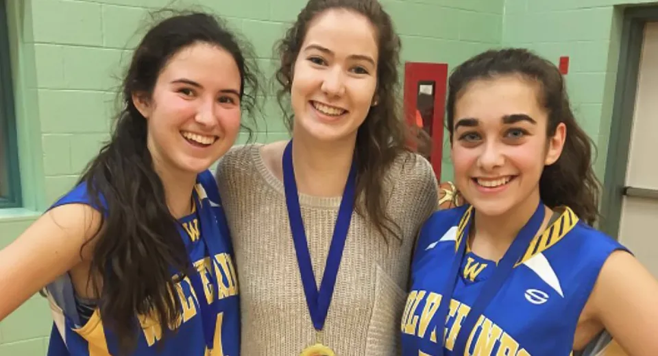 Tre studentesse in divisa sportiva blu mettono in posa davanti a una parete verde nel campus della Kensington Intermediate Senior High School.