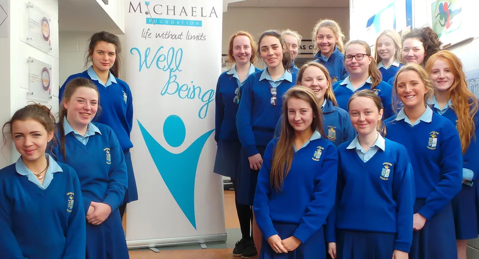 Studenti della Ursuline Secondary School Thurles davanti a una parete con le scritte 'Michaela' e 'Well being'.