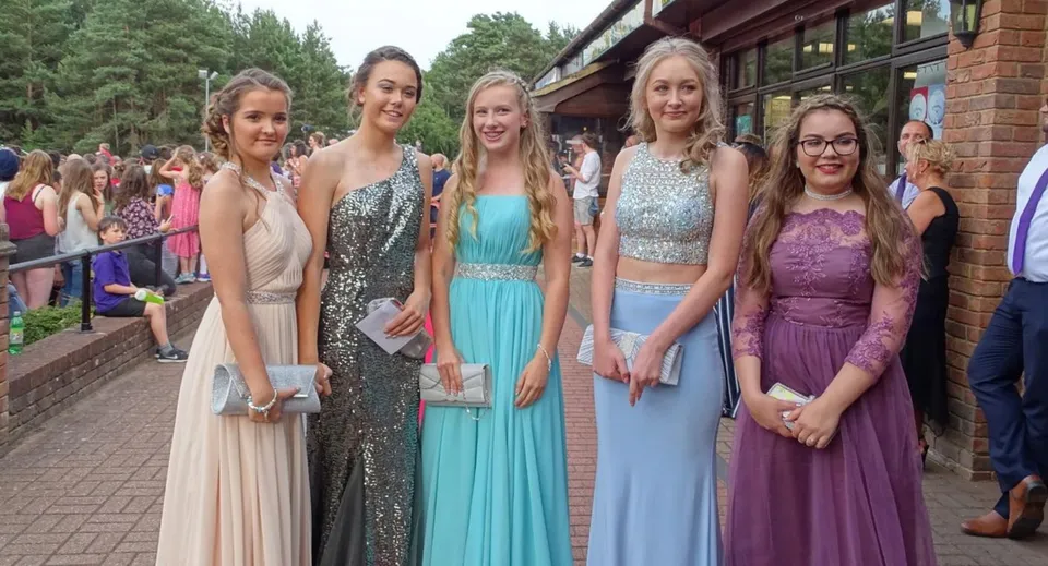 Un gruppo di studentesse del Carmel College in abito formale è davanti a un edificio in mattoni durante un evento celebrativo.