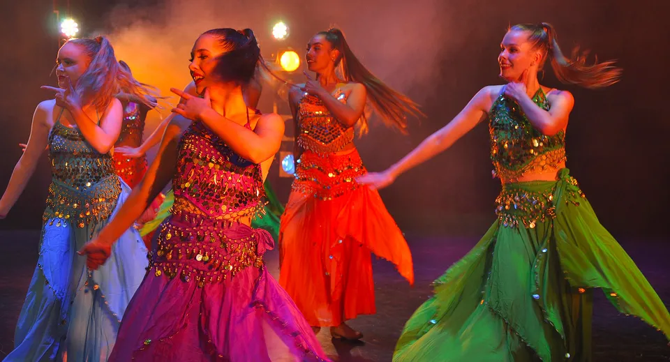 Quattro studentesse della Takapuna Grammar School si esibiscono su un palco con un'illuminazione scenografica indossando abiti colorati.
