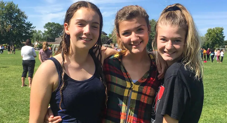 Tre studentesse si trovano su un'area erbosa davanti ad alcuni alberi nel campus del Northern Collegiate Institute & Vocational School.