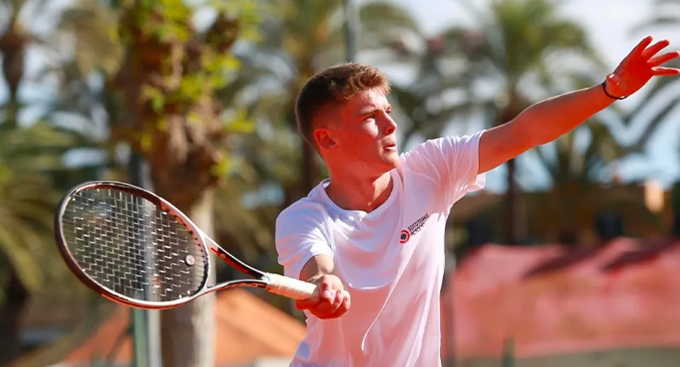 Una persona tiene una racchetta da tennis durante un colpo davanti a delle palme nel campus della Sotogrande International School.