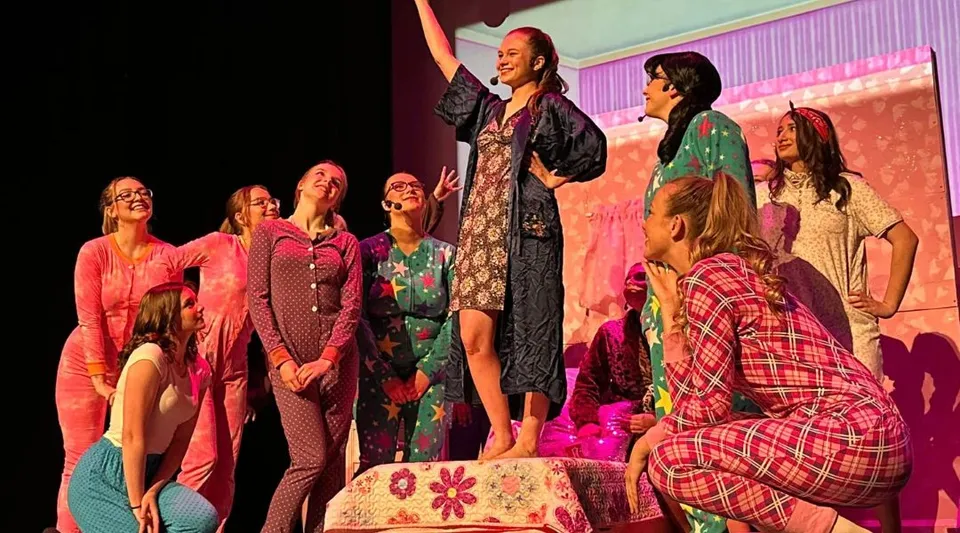 Gli studenti della Chateauguay Valley Regional High School sono su un palco con abiti colorati davanti a uno sfondo a fantasia.