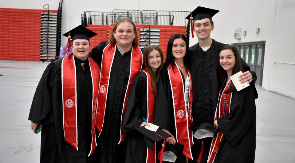 Un gruppo di laureati della SUNY Plattsburgh è insieme in toghe accademiche rosse e nere e festeggia la propria laurea.