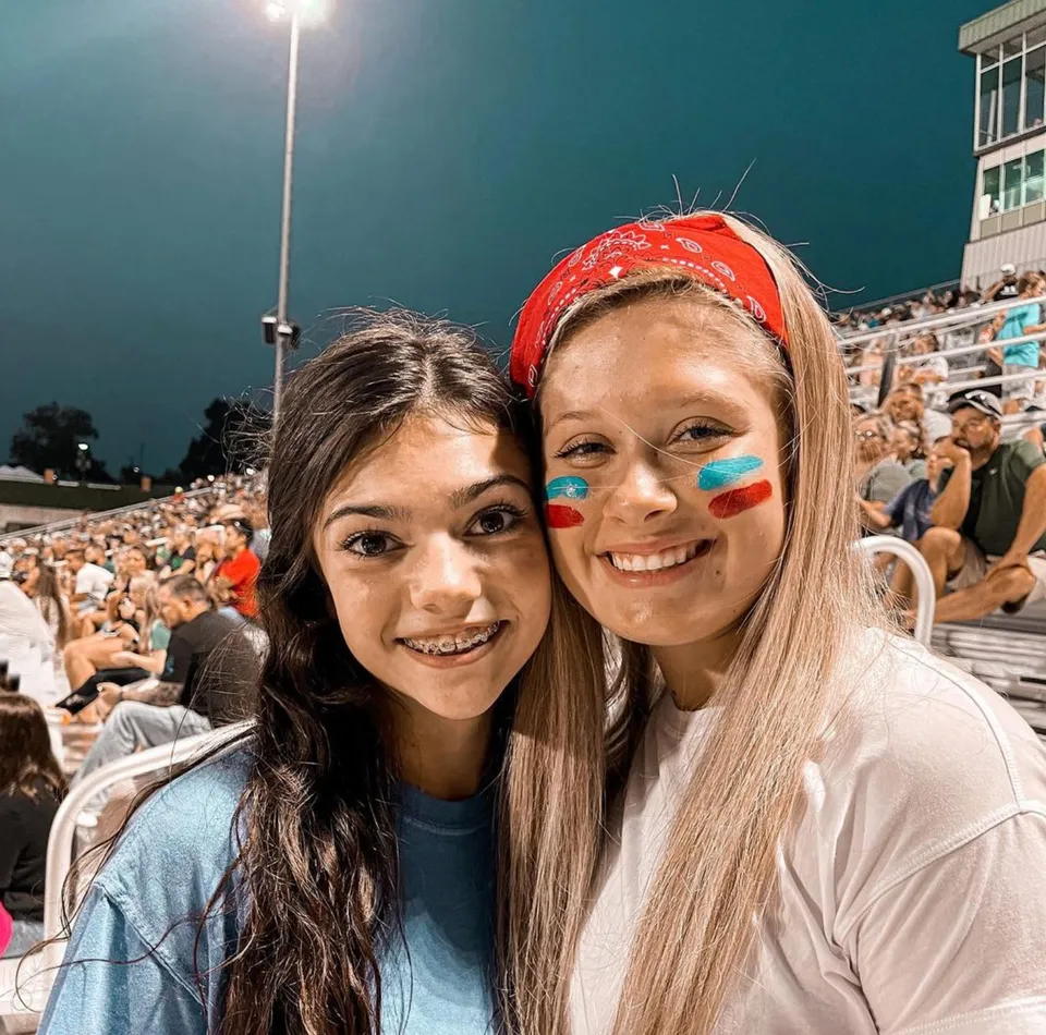 Due studentesse della Alma High School in posa nello stadio gremito con numerosi spettatori sullo sfondo.