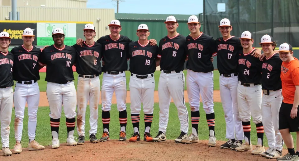 Studenti della Cathedral Preparatory School in uniforme da baseball con casco sul campo da baseball davanti a un edificio.