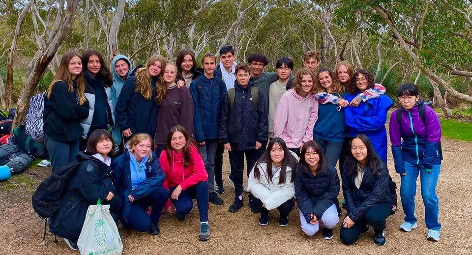 Un gruppo di studenti della Hallett Cove School si trova in un'area boschiva con alberi alti e fitta vegetazione.