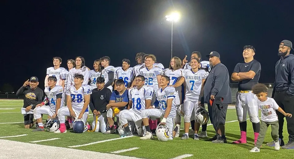 Un gruppo di giovani calciatrici e calciatori posa di notte sul campo da calcio illuminato della Sequoia Charter High School.
