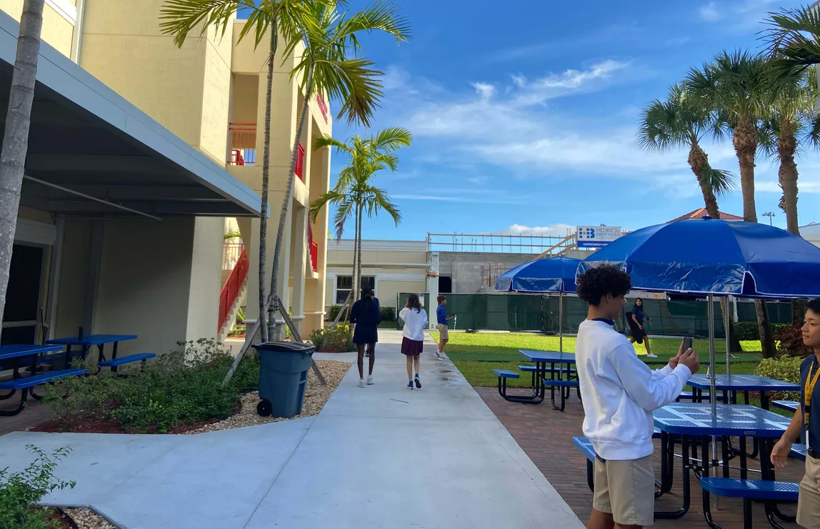Schüler:innen auf dem Campus-Hof einer Schule in Florida, mit Palmen, blauen Sonnenschirmen und Picknicktischen