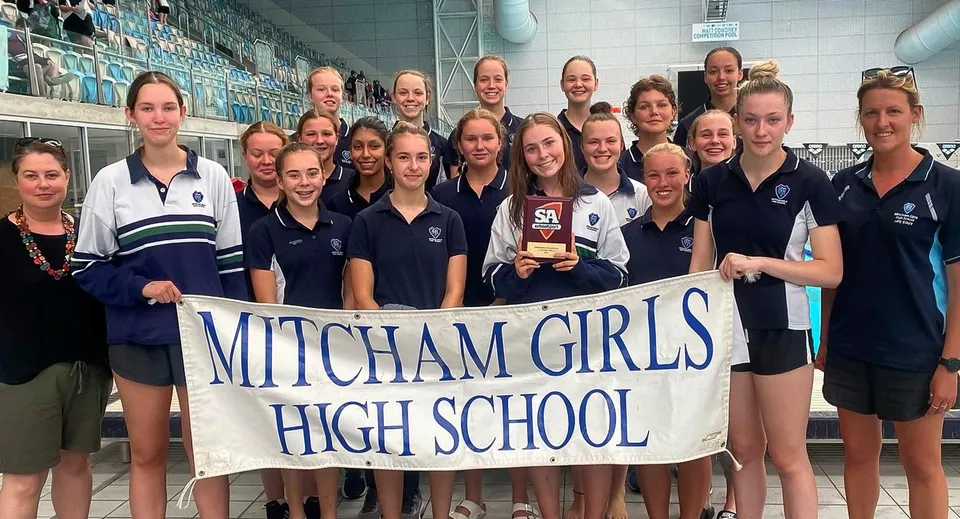 Un gruppo di studentesse della Mitcham Girls High School tiene uno striscione in una palestra.