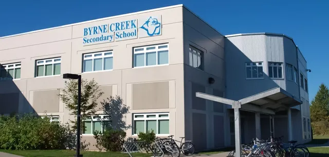 Das mehrstöckige Schulgebäude der Byrne Creek School ist von Bäumen umgeben und Fahrräder stehen davor.