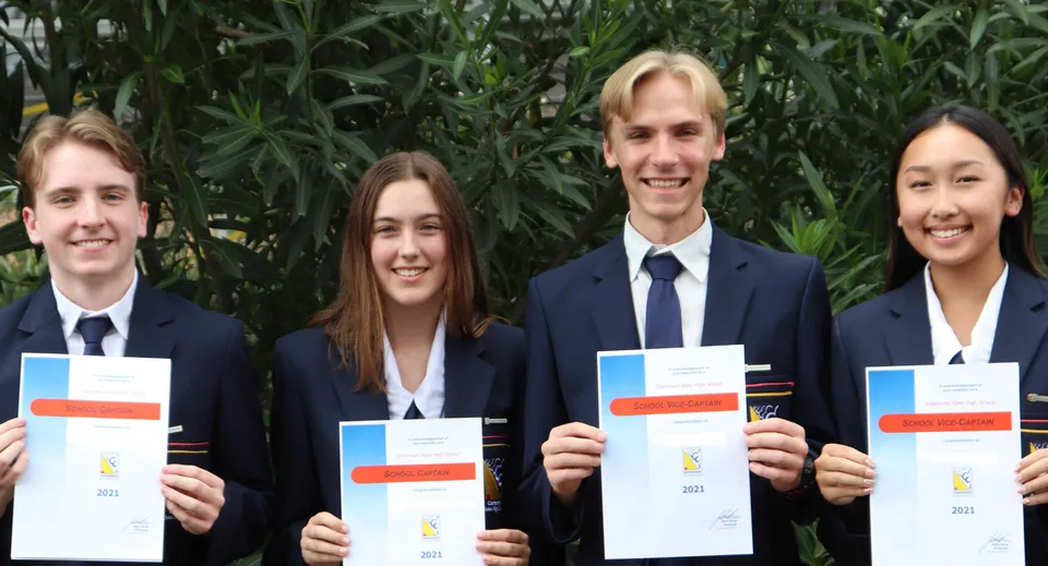 Quattro studenti della Centenary State High School tengono in mano i loro diplomi davanti a uno sfondo verde.