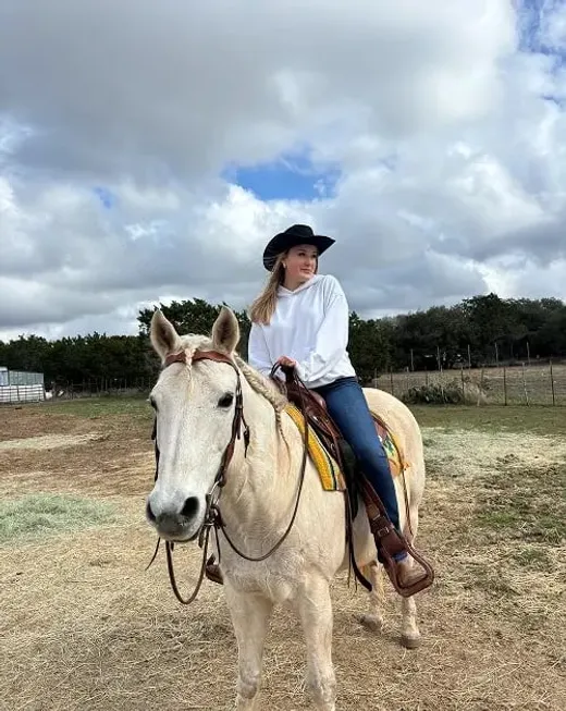 Studentessa con cappello da cowboy in sella a un cavallo bianco in un ranch negli Stati Uniti