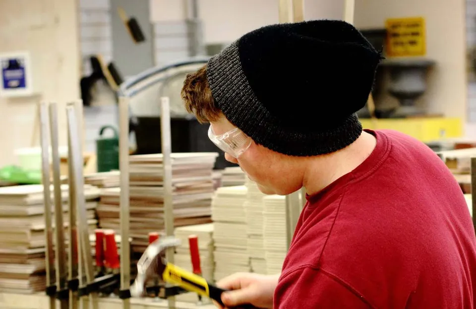 Una persona con una camicia rossa e un cappello nero si trova in una stanza con molte scatole di cartone nel Don Mills Collegiate Institute.