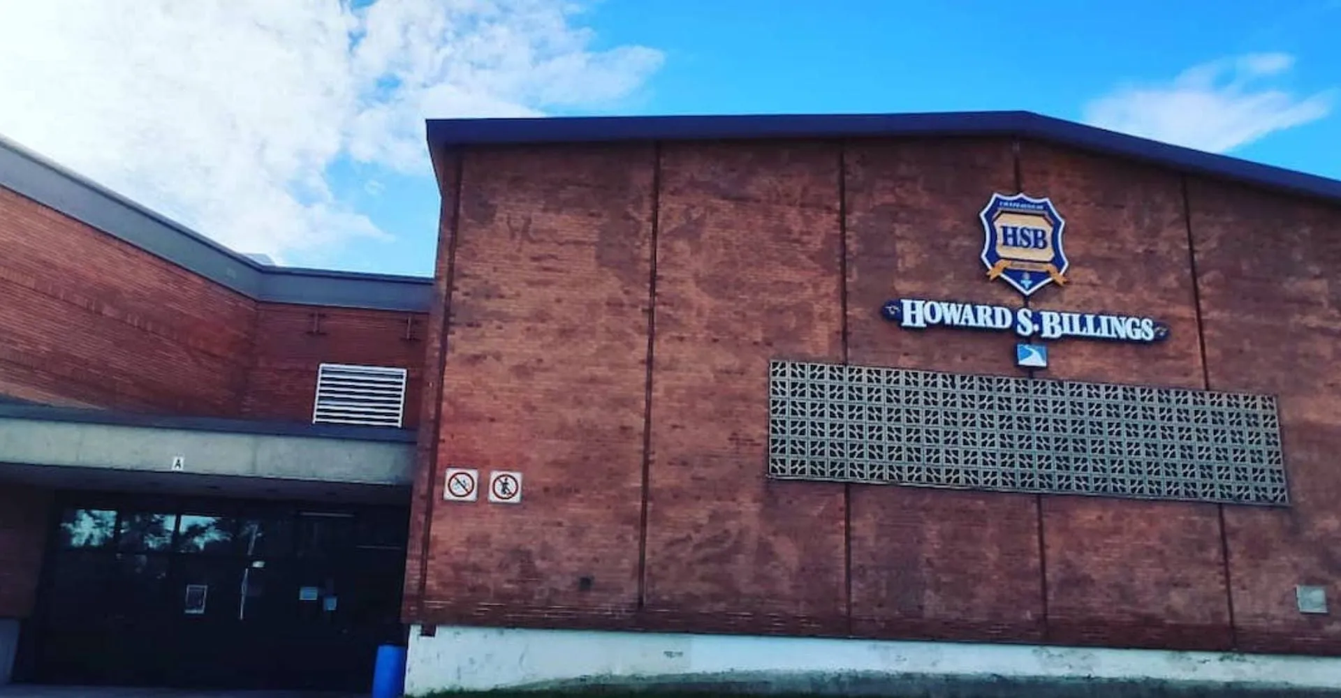 Il grande edificio in mattoni della Howard S. Billings High School con il logo sulla facciata sotto un cielo blu.